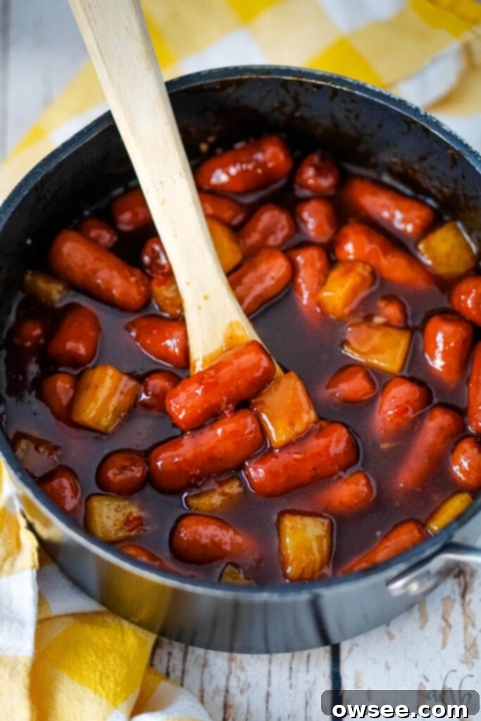 Hawaiian Little Smokies 2 A pot of Hawaiian Lit'l Smokies stirred with a wooden spoon, showcasing the sweet and spicy sauce and pineapple chunks.