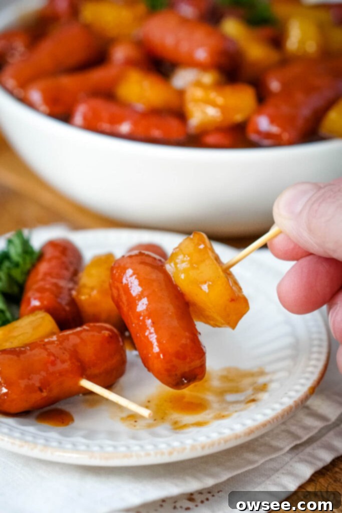 Hawaiian Little Smokies 4 Toothpick skewers of Hawaiian Lit'l Smokies and a pineapple chunk on a white plate, perfect for serving.