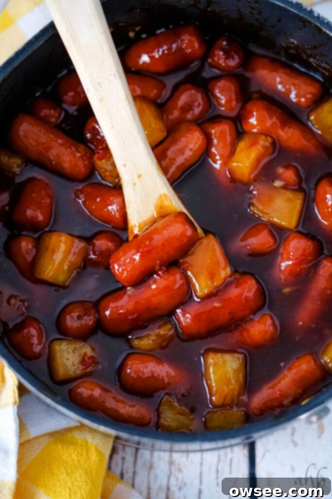 Hawaiian Little Smokies 8 A pot of Hawaiian Lit'l Smokies stirred with a wooden spoon, simmering in the sauce.