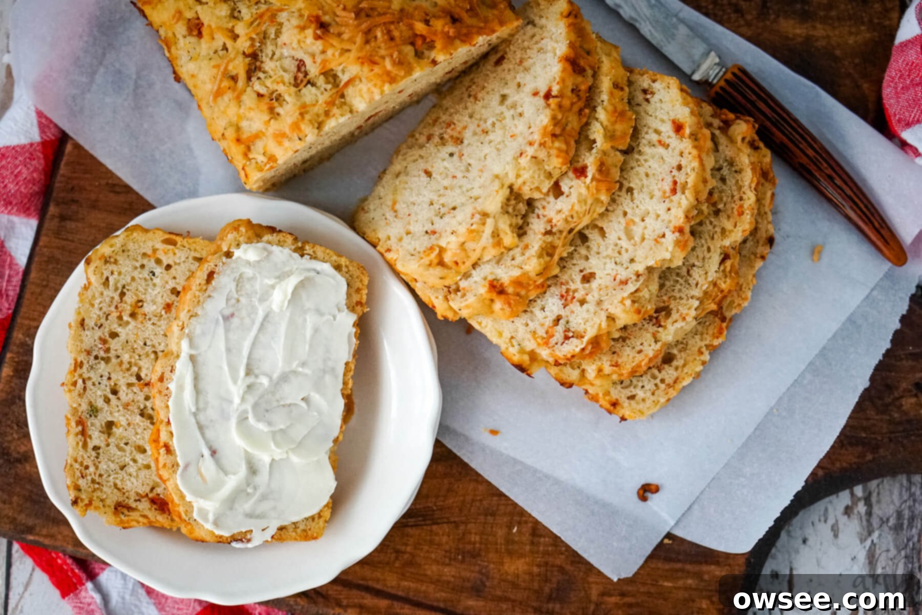 Sun-Kissed Tomato Parmesan Beer Bread 5 A beautifully sliced loaf of Sun-dried Tomato and Parmesan Beer Bread, with two slices served on a white plate with cream cheese, showcasing the vibrant ingredients.