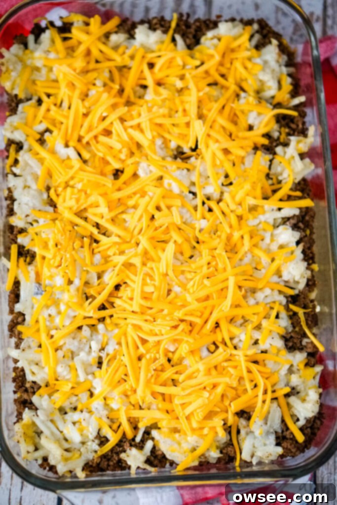 Savory Beef and Hashbrown Bake 11 The remaining shredded cheddar cheese is sprinkled generously over the partially baked casserole after the foil has been removed, ready for the final bake.