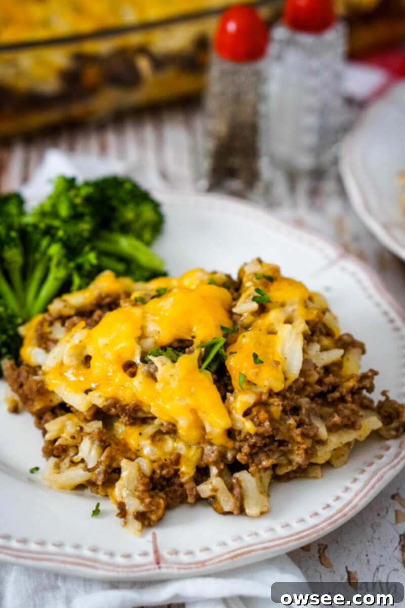 Savory Beef and Hashbrown Bake 12 A generous serving of Hamburger Hashbrown Casserole with vibrant green cooked broccoli on a white plate, showcasing a perfect family meal.