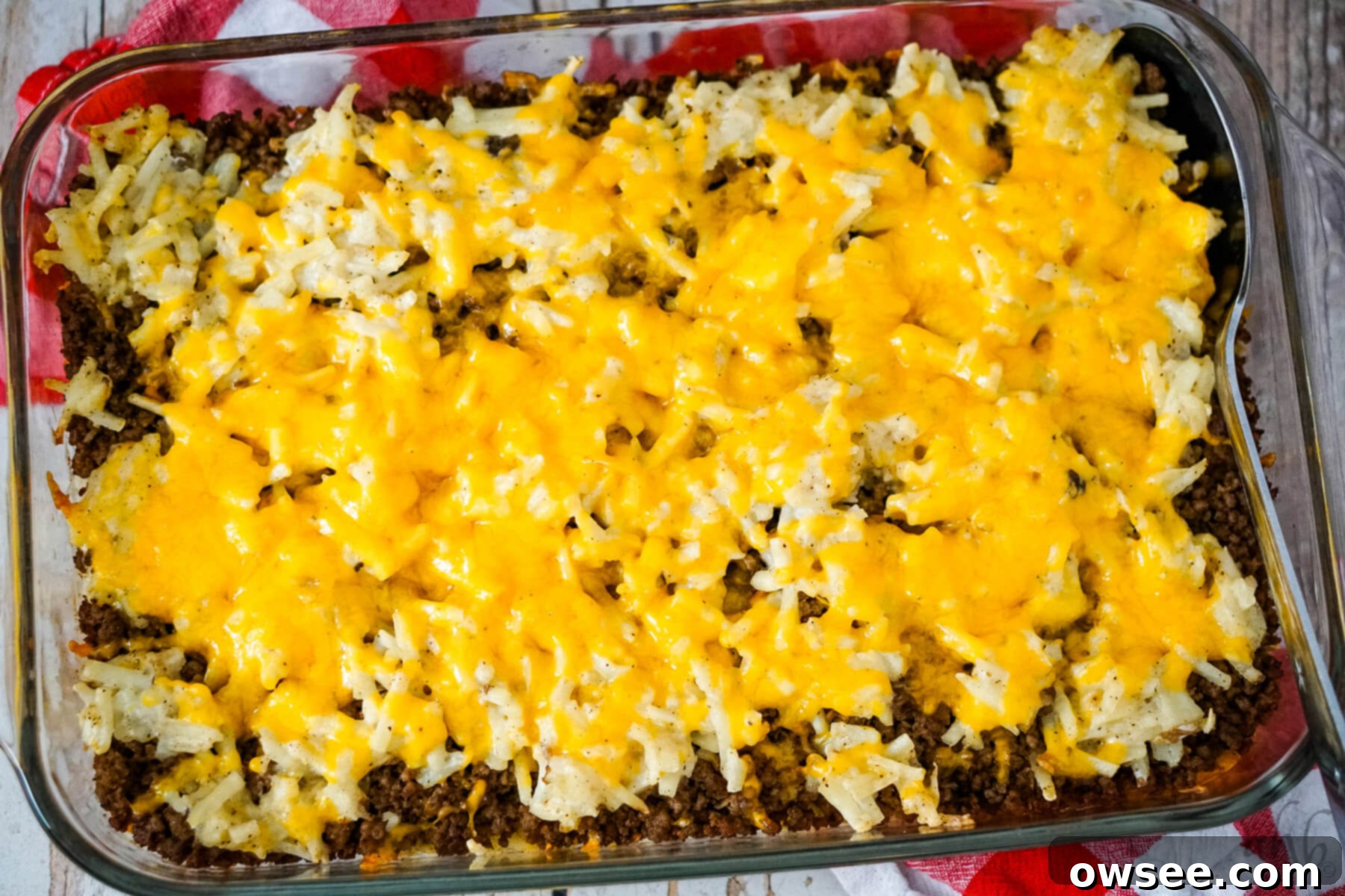 Savory Beef and Hashbrown Bake 4 A large rectangular pan of golden-brown Hamburger Hashbrown Casserole, freshly baked and ready to serve, with a spoon to one side.