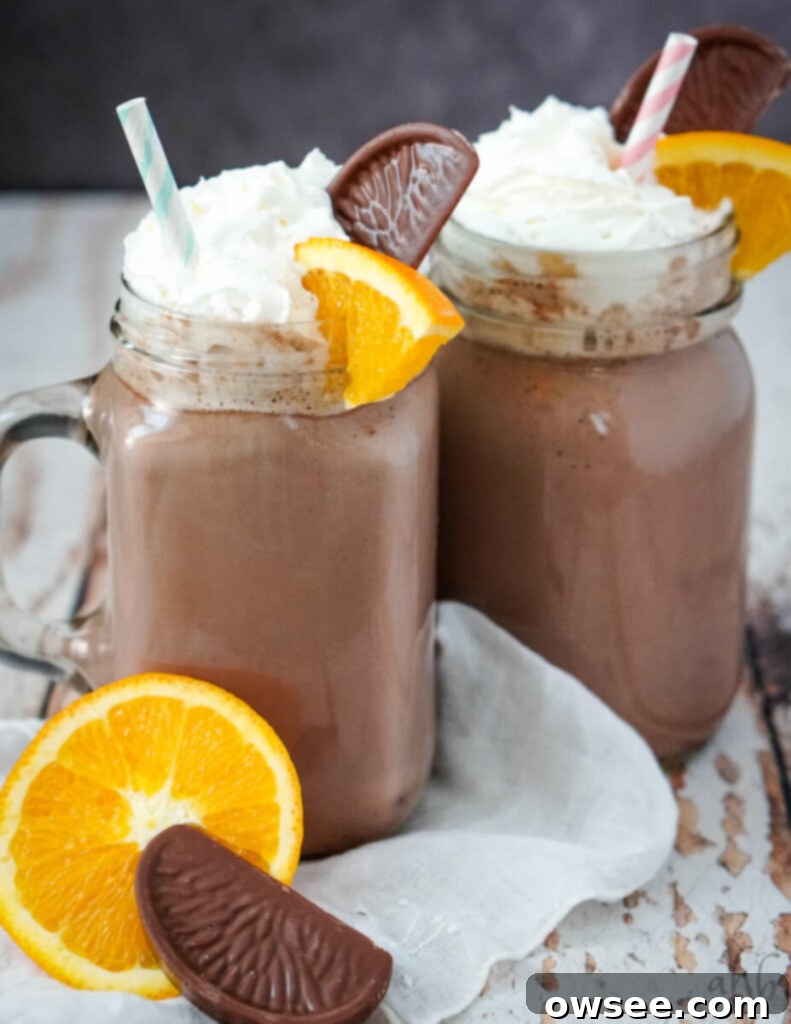 Zesty Cocoa Bliss 4 Clear glass mugs full of orange hot chocolate with colorful striped straws. An orange and a chocolate bar rest in front of the mugs on a wooden surface.