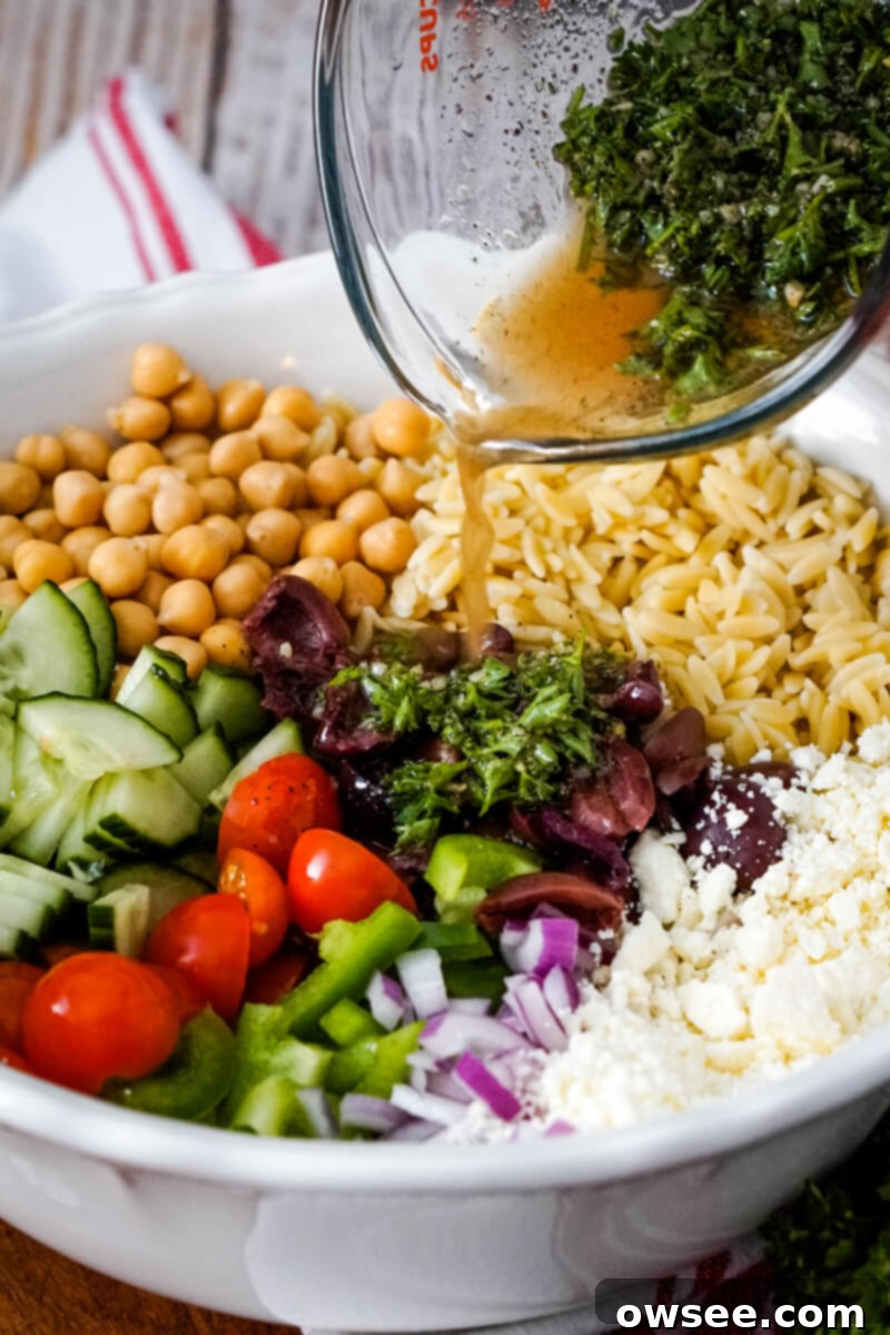 Zesty Orzo Chickpea Salad 5 All the vibrant ingredients of the Orzo Garbanzo Bean Salad are added to a large white bowl while the homemade dressing is poured over them, ready for mixing.