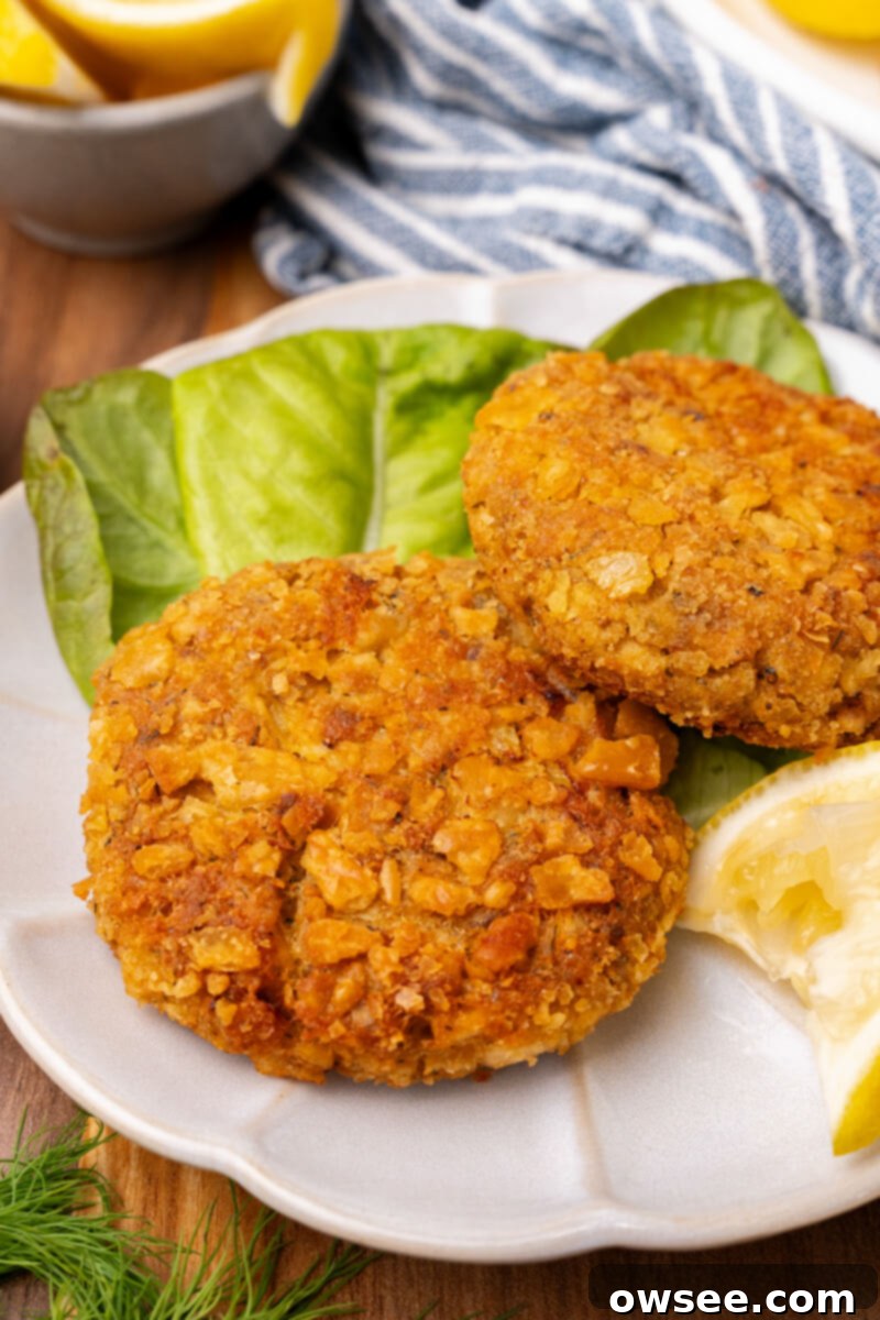 Grandma's Homestyle Salmon Patties 3 Two golden salmon patties served on a white plate with a fresh leaf of lettuce and a bright lemon slice.