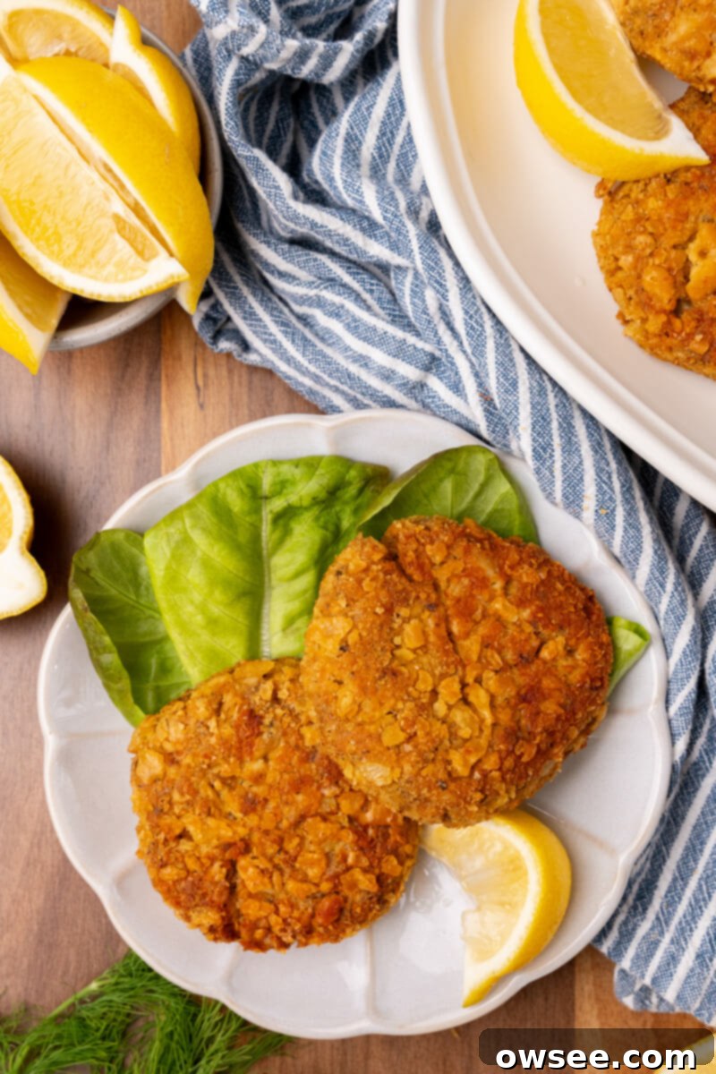 Grandma's Homestyle Salmon Patties 4 A white plate with two perfectly fried salmon patties and a wedge of lemon to one side, ready to be served.