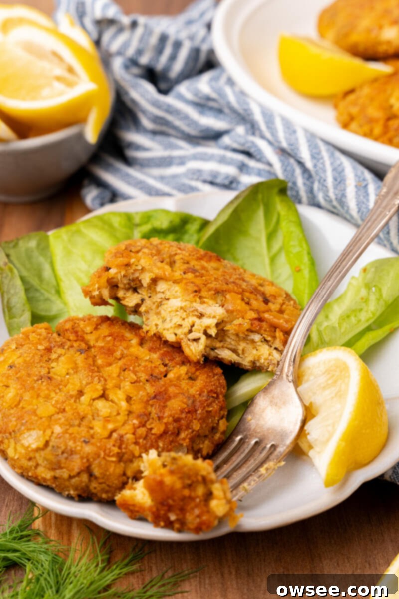 Grandma's Homestyle Salmon Patties 9 A plate of two golden-brown salmon patties served with a crisp lettuce leaf and a lemon slice. One patty is half-eaten, with a fork taking a bite-sized piece, showcasing its tender interior.