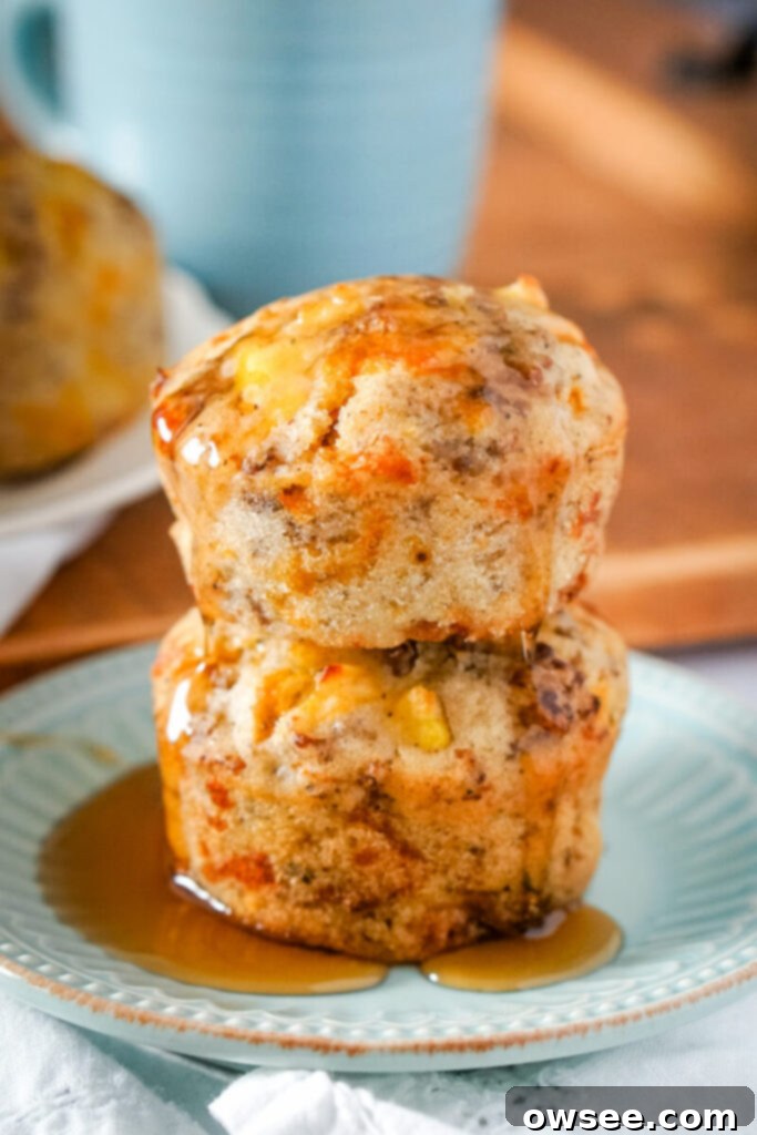 All-in-One Breakfast Muffins 2 Two McGriddle muffins are stacked on a light blue plate and covered in syrup. The muffins are golden brown with bits of sausage and cheese visible.