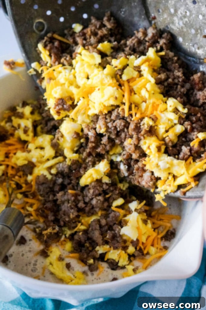 All-in-One Breakfast Muffins 6 A mixture of browned sausage crumbles, broken up scrambled eggs, and shredded cheddar cheese is being added to a bowl of pancake mix, ready to be combined.