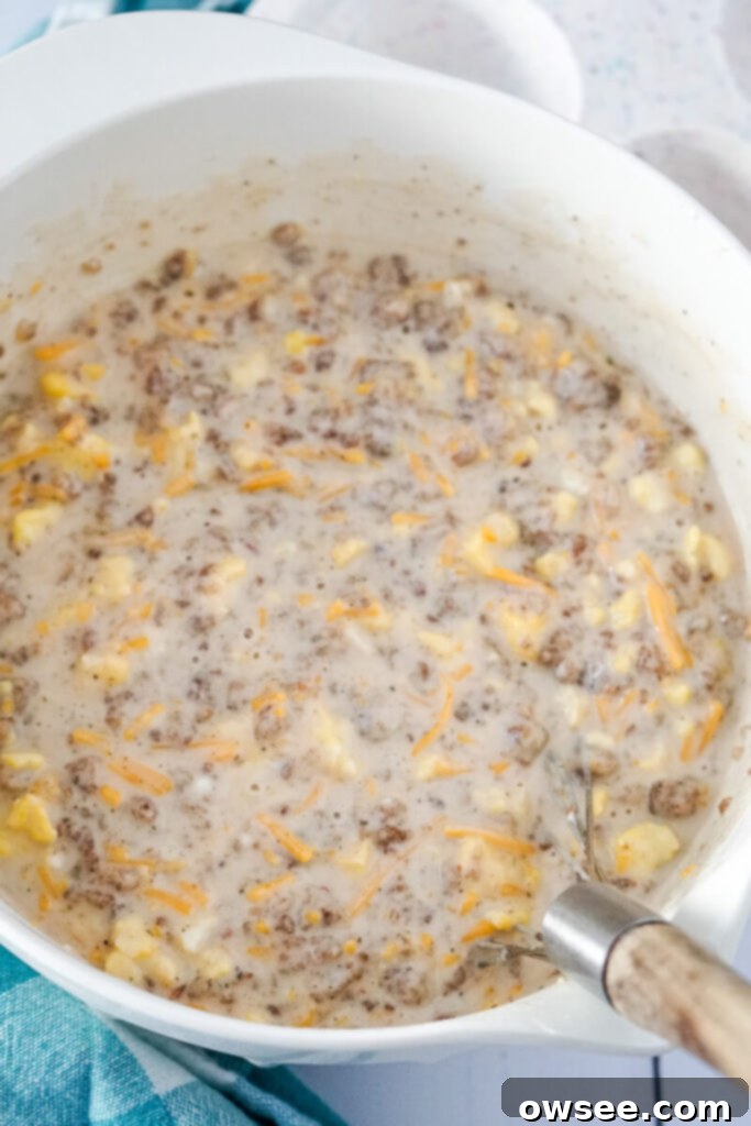 All-in-One Breakfast Muffins 7 The pancake batter mixture, now combined with sausage, eggs, and cheese, is being stirred thoroughly with a whisk in a large mixing bowl.