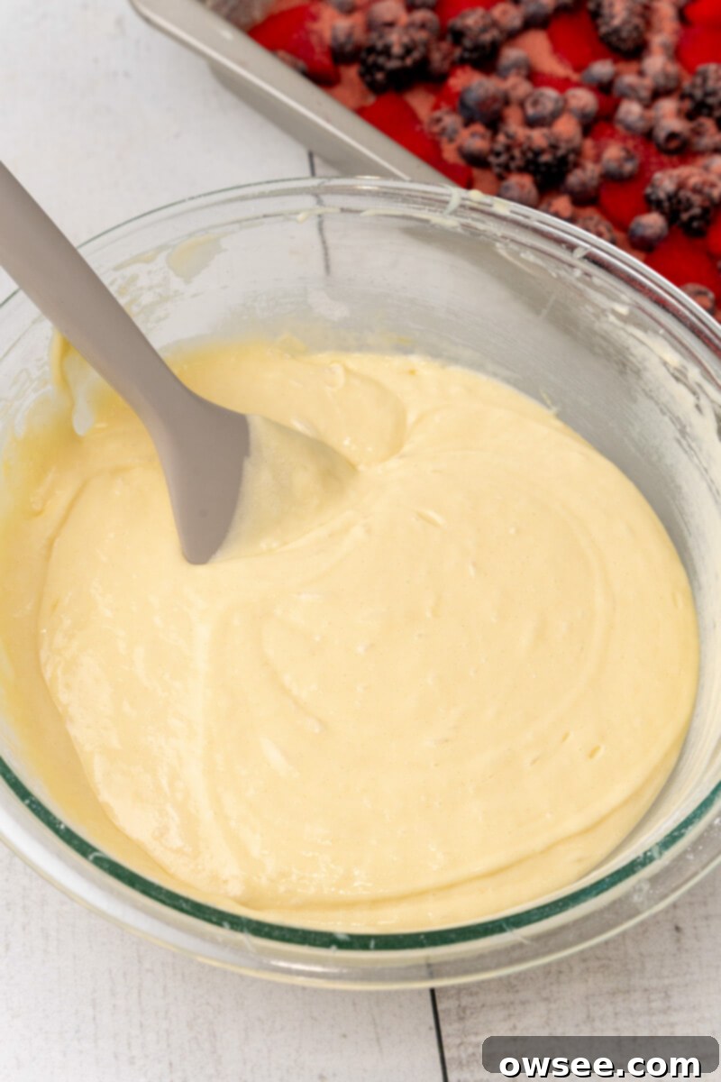 Caramelized Berry Flip Cake 7 All the cake mix ingredients, including the boxed mix, water, vegetable oil, eggs, and Greek yogurt, are combined and mixed together in a clear glass mixing bowl.