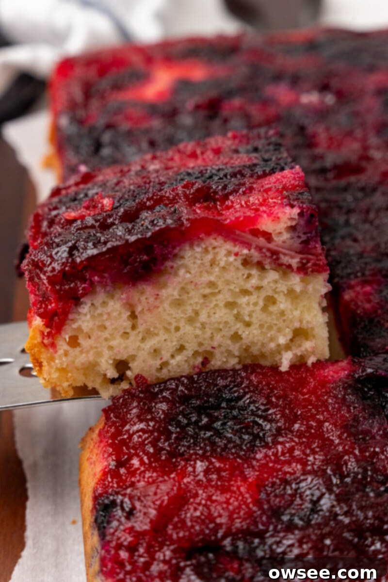 Caramelized Berry Flip Cake 10 A generous slice of the Berry Upside Down Cake, showing its vibrant berry topping and moist yellow cake, is being lifted out of the pan with a cake server, ready to be served.