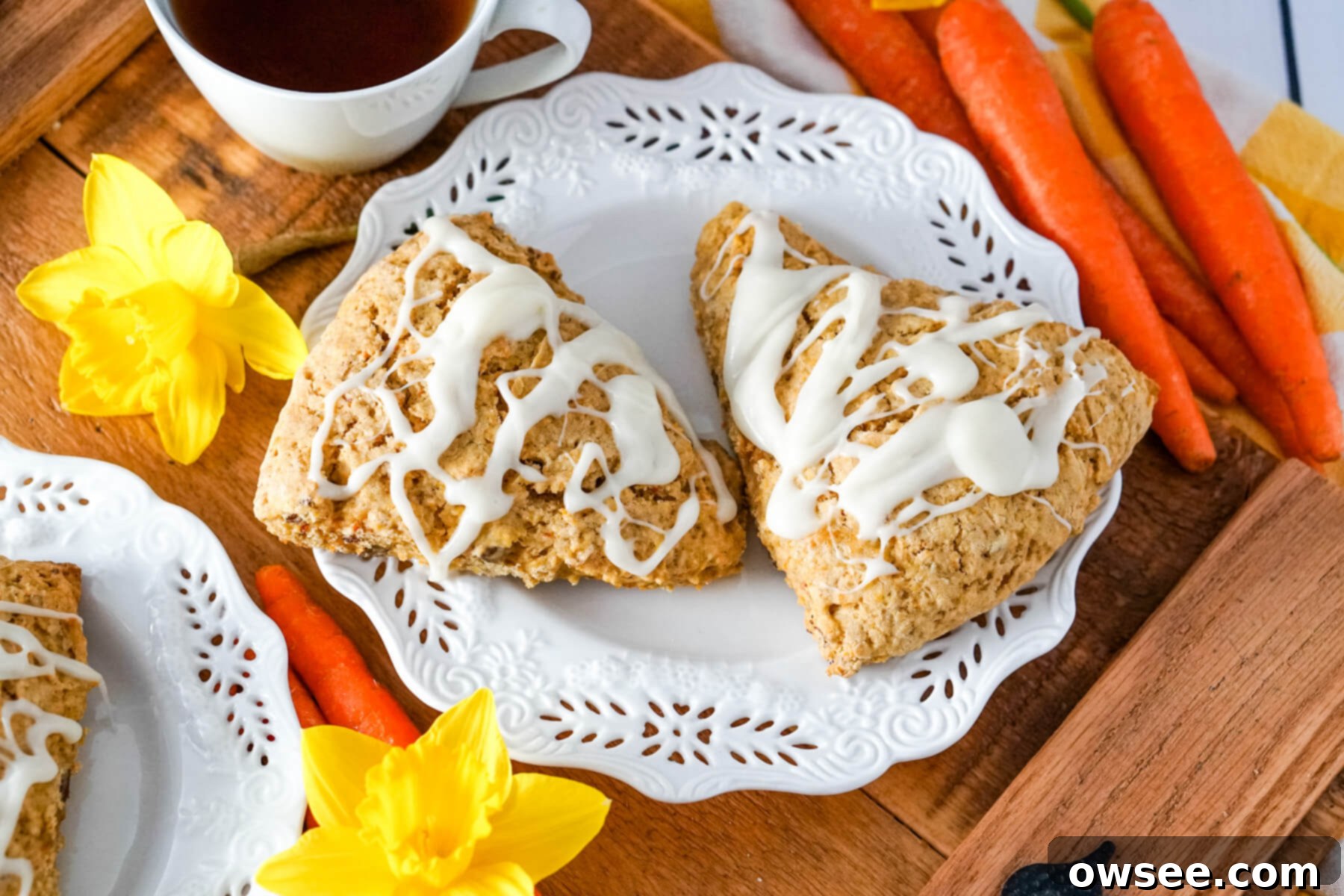 Effortless Carrot Cake Scones 2 Two scones are served on a decorative white plate next to yellow flowers and carrots.