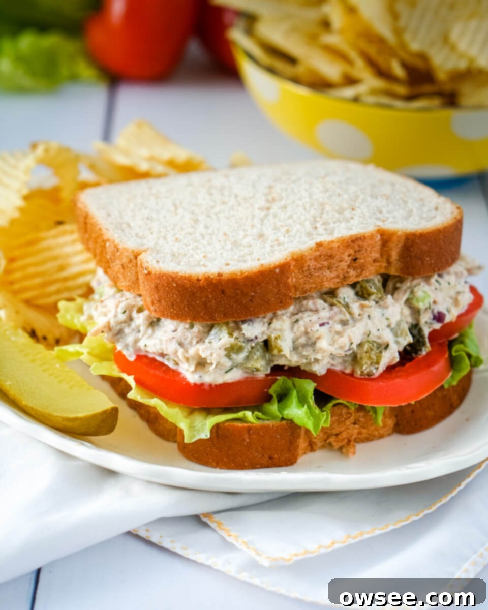 Dill-icious Tuna Salad 6 A delectable Dill Pickle Tuna Salad Sandwich, garnished with a side pickle and potato chips, presented on a pristine white plate.