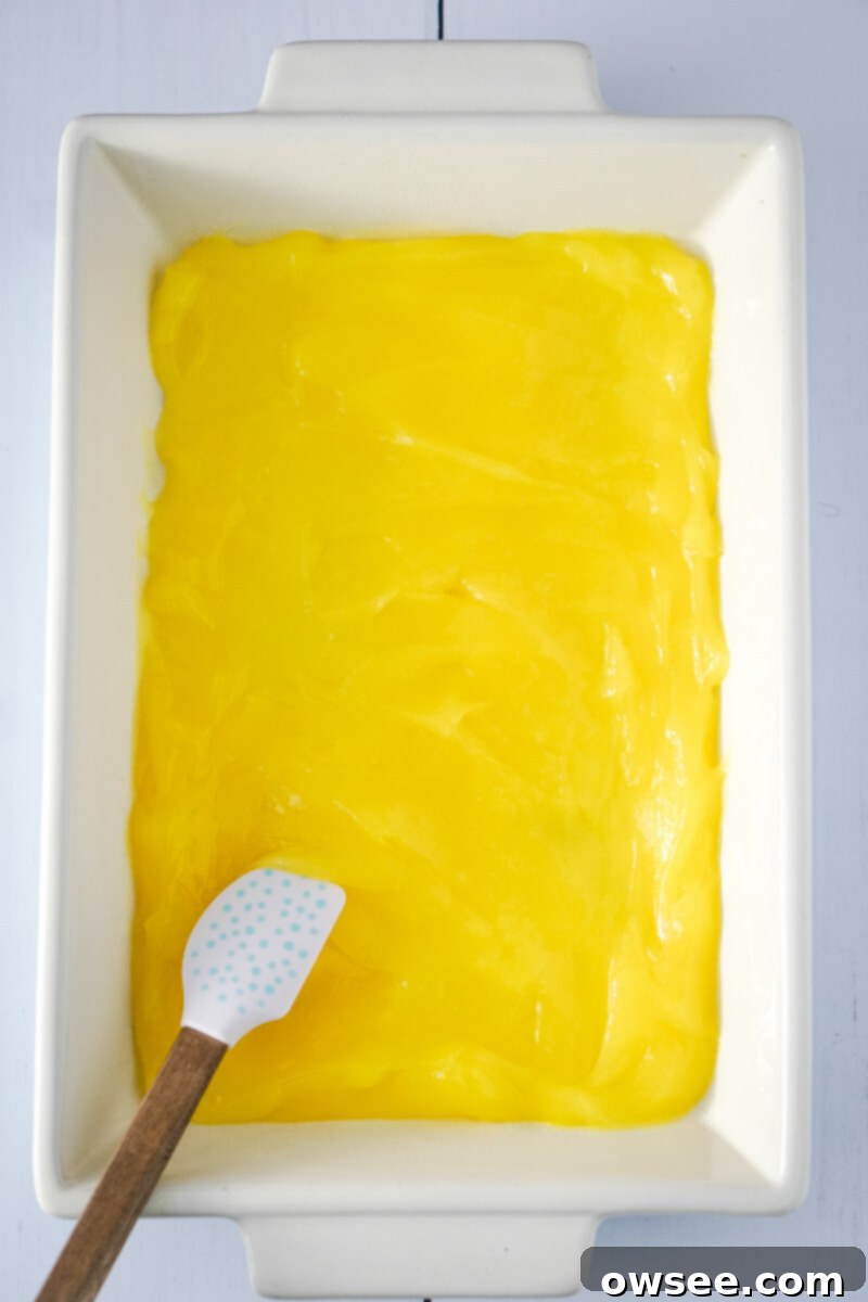 Zesty Lemon Dump Cake 5 The vibrant lemon pie filling is smoothly spread out in the bottom of a glass baking pan, ready for the next layer.