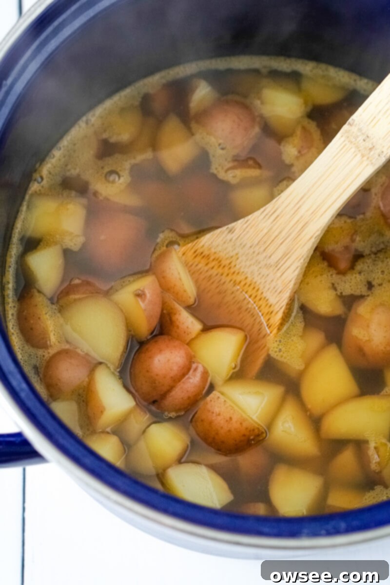 Unbelievably Easy 3 Ingredient Potato Soup 5 A stock pot filled with vegetable broth and bite sized pieces of baby red potatoes is stirred with a wooden spoon.