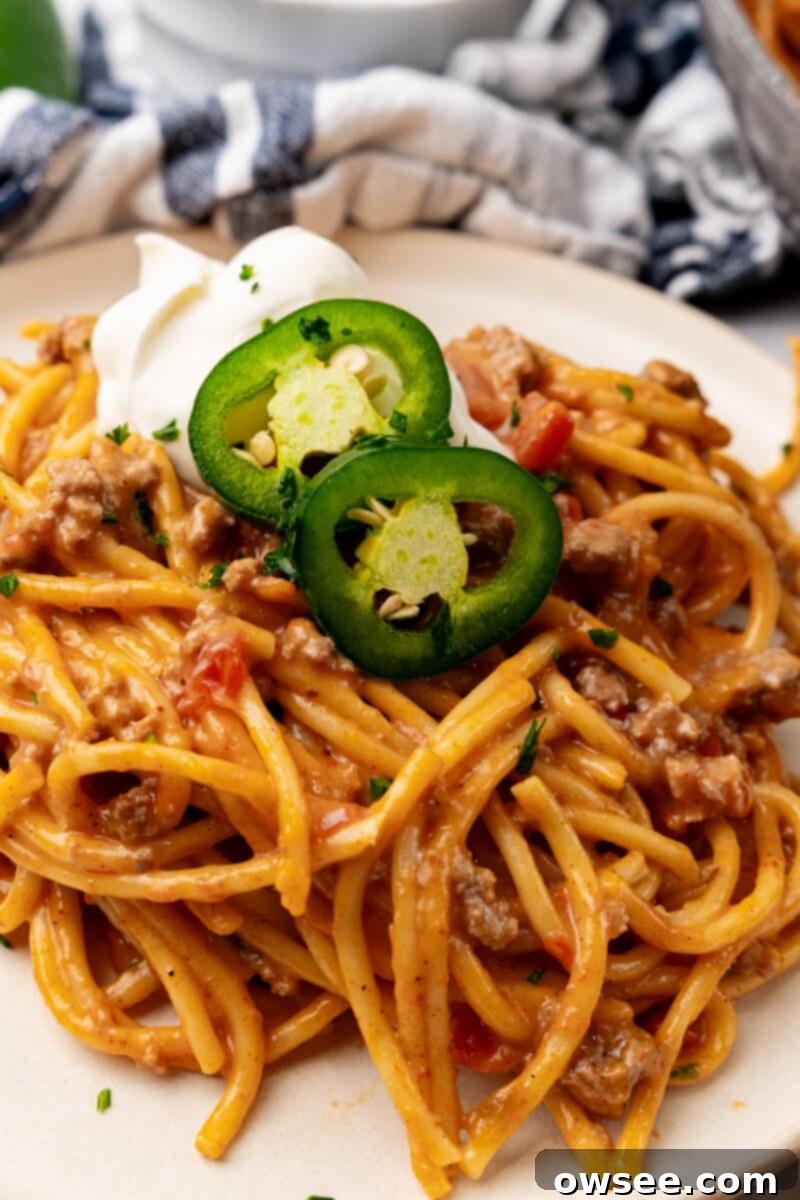 Taco Spaghetti Fiesta 2 A vibrant serving of Cheesy Taco Spaghetti on a white plate, beautifully garnished with fresh cilantro, a dollop of sour cream, and two fiery jalapeño slices, ready to be enjoyed.