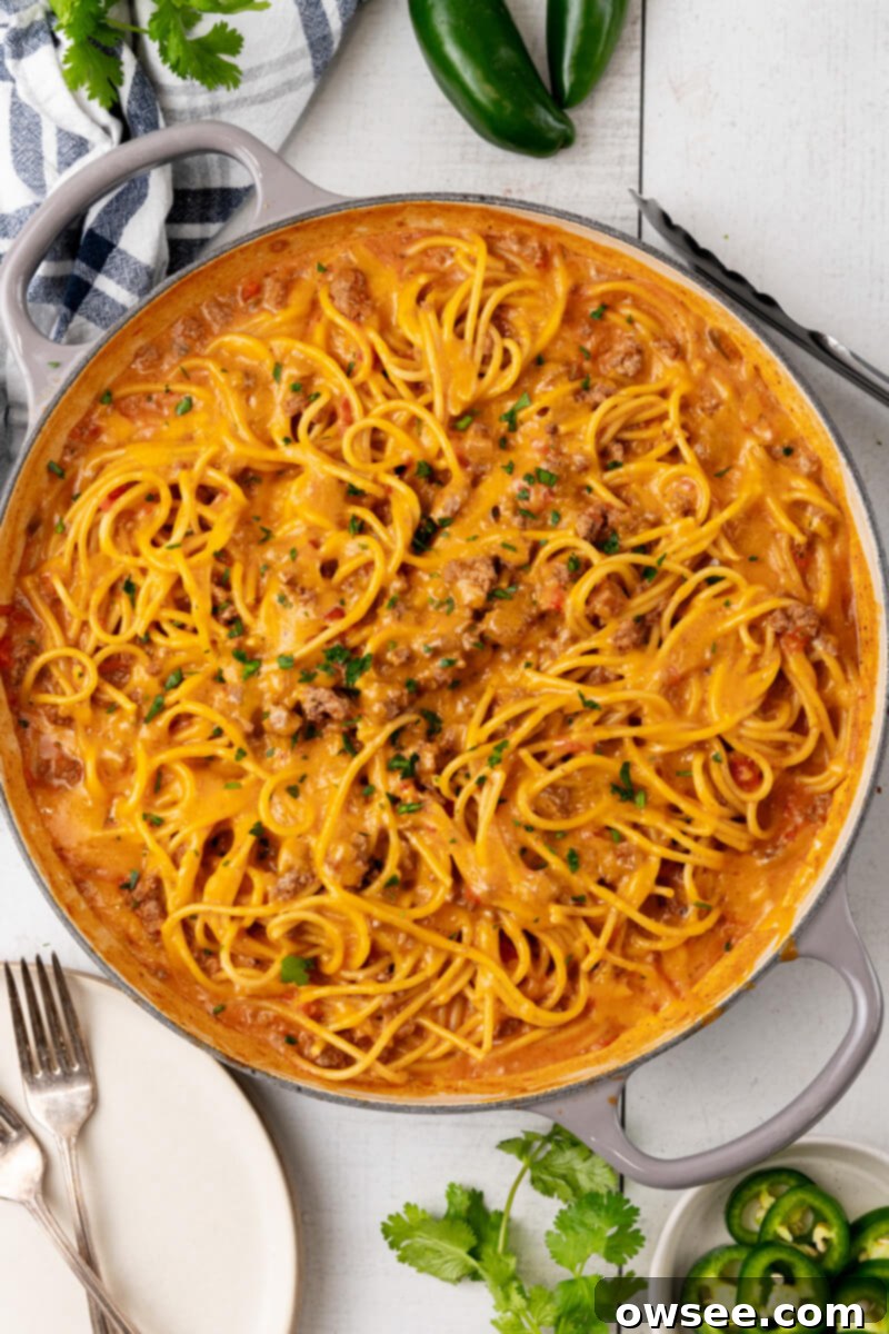 Taco Spaghetti Fiesta 11 A large skillet brimming with hot, cheesy taco spaghetti, perfectly melted cheddar cheese, and a generous topping of fresh chopped cilantro, ready to be served as a delicious meal.