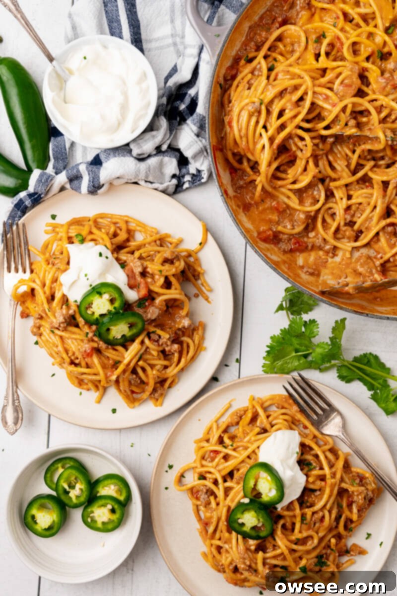 Taco Spaghetti Fiesta 3 Two generously portioned servings of Cheesy Taco Spaghetti, complete with an array of fresh toppings, presented on white plates alongside the main pot of creamy, cheesy taco spaghetti, highlighting its appeal for family meals.