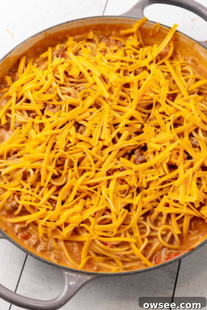 Taco Spaghetti Fiesta 10 Freshly shredded cheddar cheese is sprinkled generously over the Cheesy Taco Spaghetti in the skillet, preparing for the final melting stage.