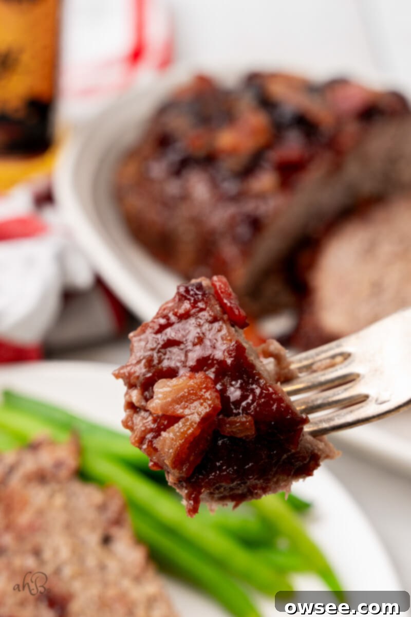 Bite of Bourbon Bacon Meatloaf A fork holds a delectable bite of bourbon bacon meatloaf, showing its tender texture and glazed exterior.