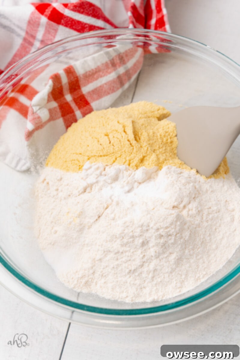 The dry ingredients for malted chocolate chip cookies, including flour, baking soda, salt, and malted milk powder, are mixed together in a clear glass bowl.