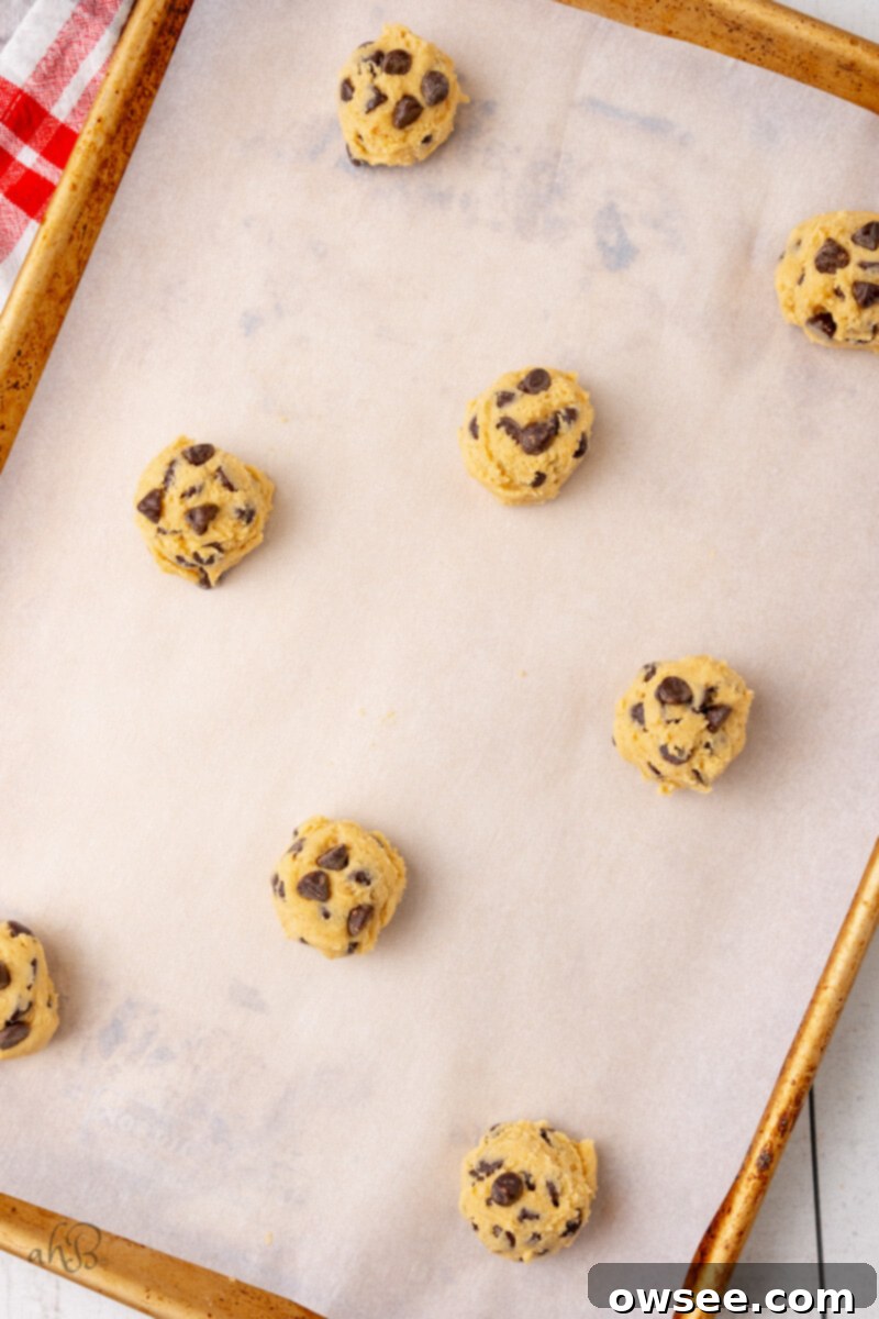 Uniform spoonfuls of Malted Chocolate Chip cookie dough are meticulously placed on a baking tray lined with parchment paper, perfectly spaced for even baking.