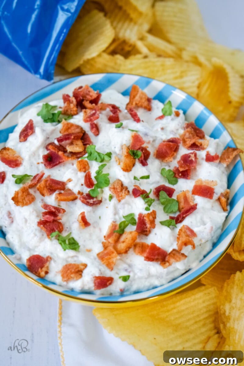 Smoky Horseradish Bacon Sensation 3 A bowl of bacon horseradish dip is served in a blue and white striped bowl and surrounded by potato chips.