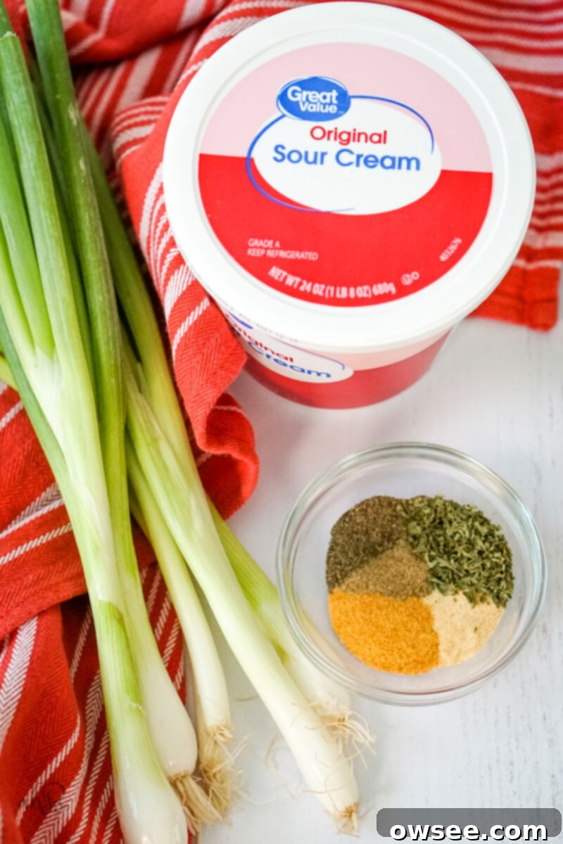 Green Onion Dip Ingredients 5 green onions, a bowl of spices, a container of sour cream, and a towel sit on a table.