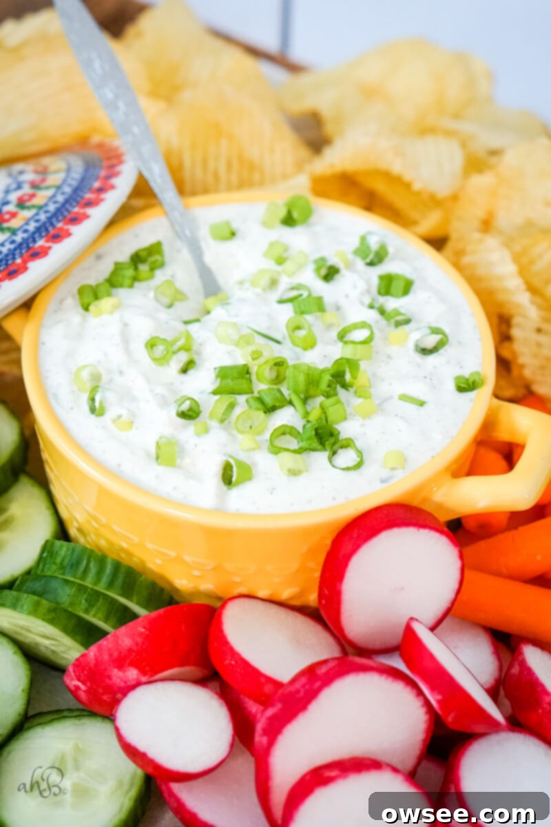 Green Onion Dip-8 A yellow dish of green onion dip is in the center of potato chips, and veggies with a lid off to the side.