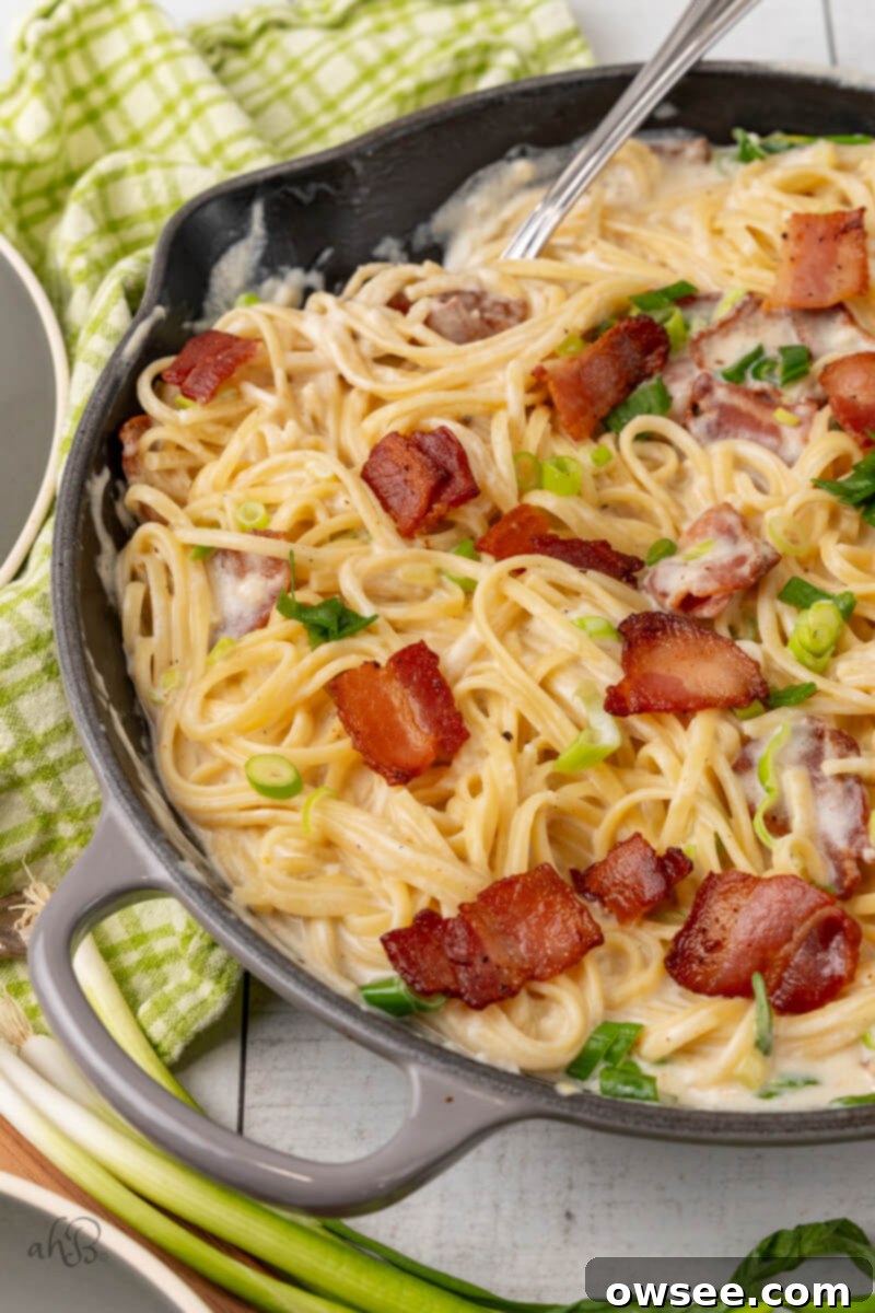 Creamy Tang Pasta 2 A skillet full of sour cream pasta stirred by a fork and topped with green onions and bacon pieces.