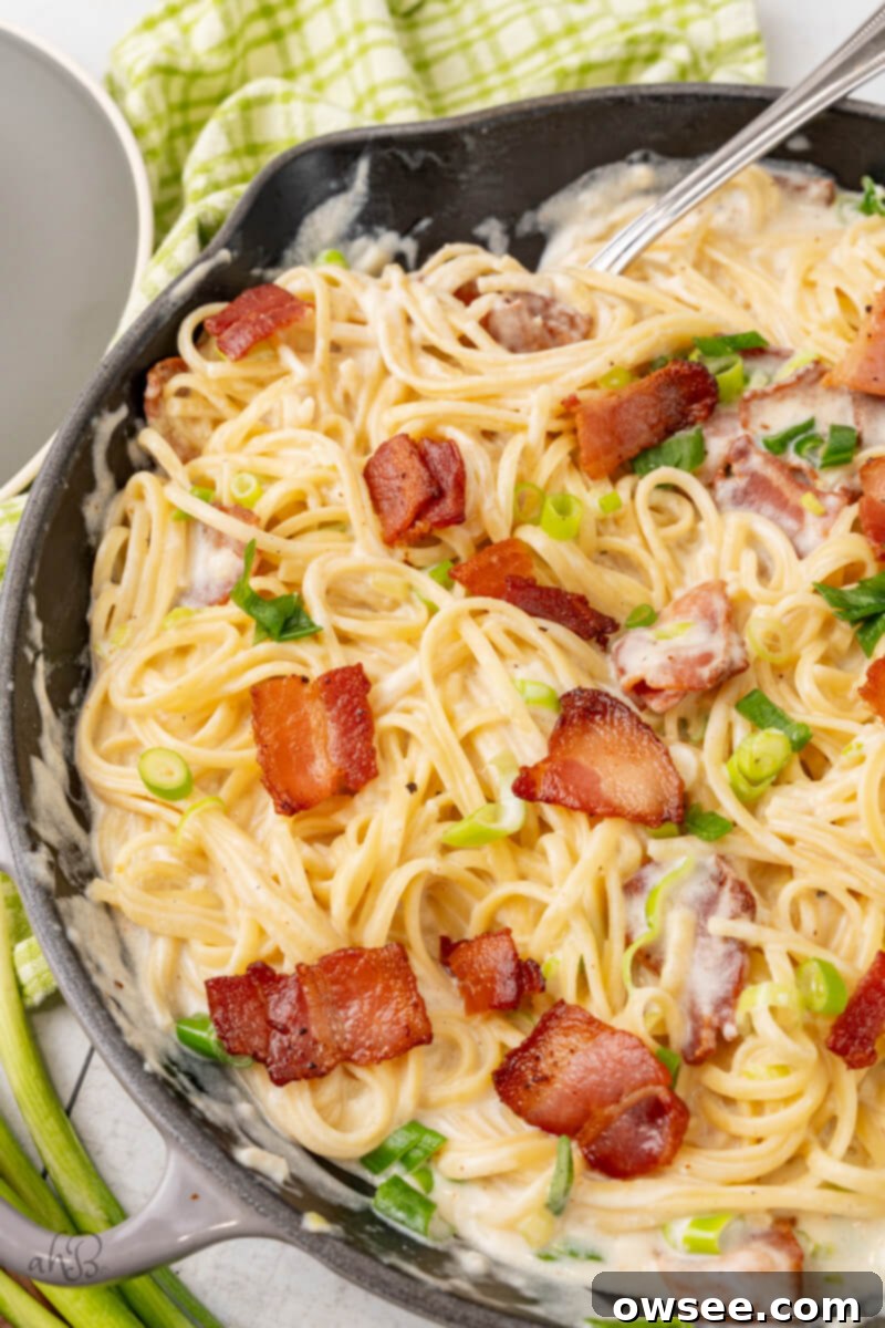 Creamy Tang Pasta 11 A skillet full of sour cream pasta stirred by a fork and topped with green onions and bacon pieces.