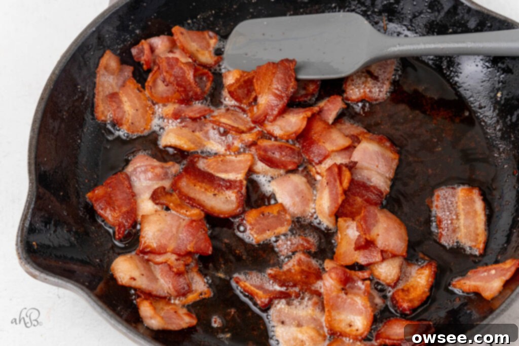 Creamy Tang Pasta 5 Bacon pieces are cooked in a skillet and stirred with a spatula.