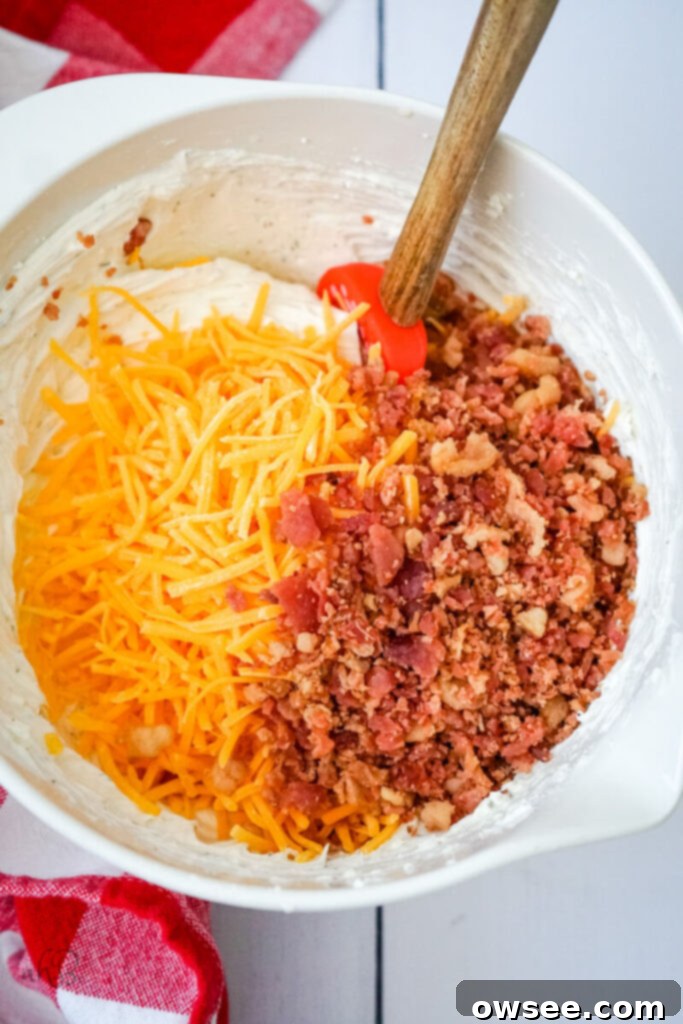 Creamy Ranch Beer Cheese Dip 8 Shredded cheddar cheese and bacon pieces are added to the creamy ranch and beer mixture in a bowl, ready to be folded in.