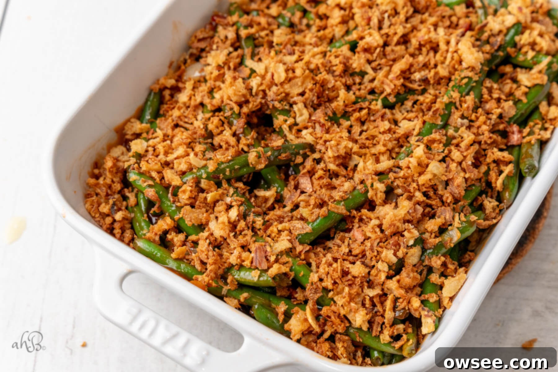 Smoky BBQ Green Bean Casserole 3 A white casserole dish is filled with BBQ Green Bean Casserole, garnished with fresh herbs and showing the crispy onion topping. Perfect for holiday meals or a comforting family dinner.