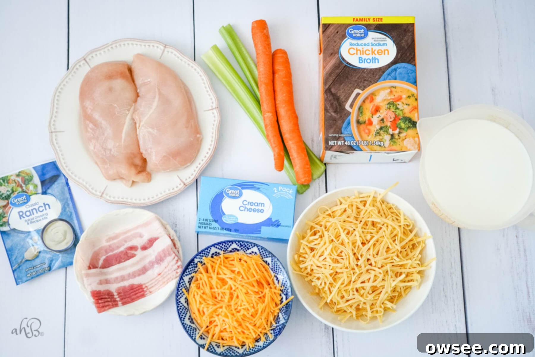 Irresistible Chicken Noodle Soup 5 Ranch seasoning packet, bacon strips, two chicken breasts, two carrots, two celery stalks, a box of cream cheese, shredded cheese, a bowl of egg noodles, milk, and a box of chicken broth.