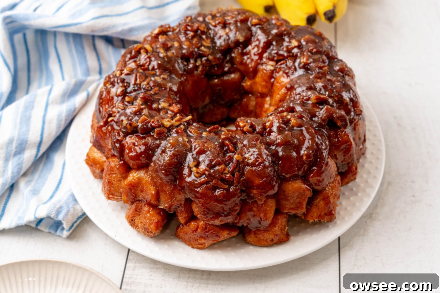 Gooey Caramel Banana Pull-Apart Bread 2 Bananas Foster Monkey Bread sits on a white plate, glistening with caramel sauce.
