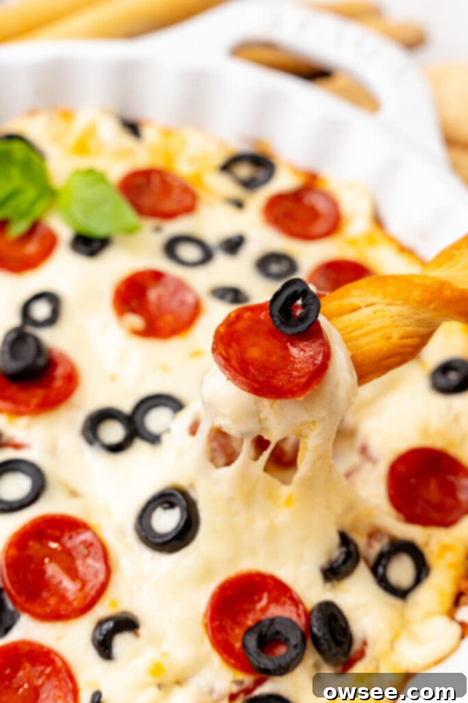 Hot Cheesy Pepperoni Dip 2 A breadstick scoops up hot melted cheesy pepperoni dip, showcasing its gooey texture and specks of pepperoni.