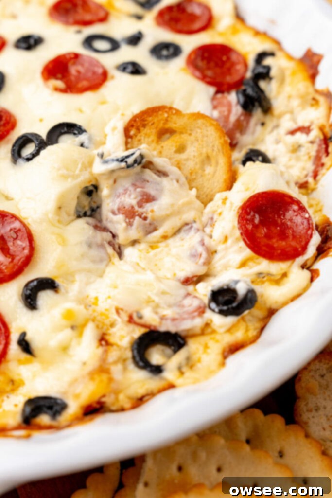 Hot Cheesy Pepperoni Dip 5 A golden-brown toast round is scooping up a generous bite of the hot, gooey, and flavorful pepperoni dip, showing its inviting texture.
