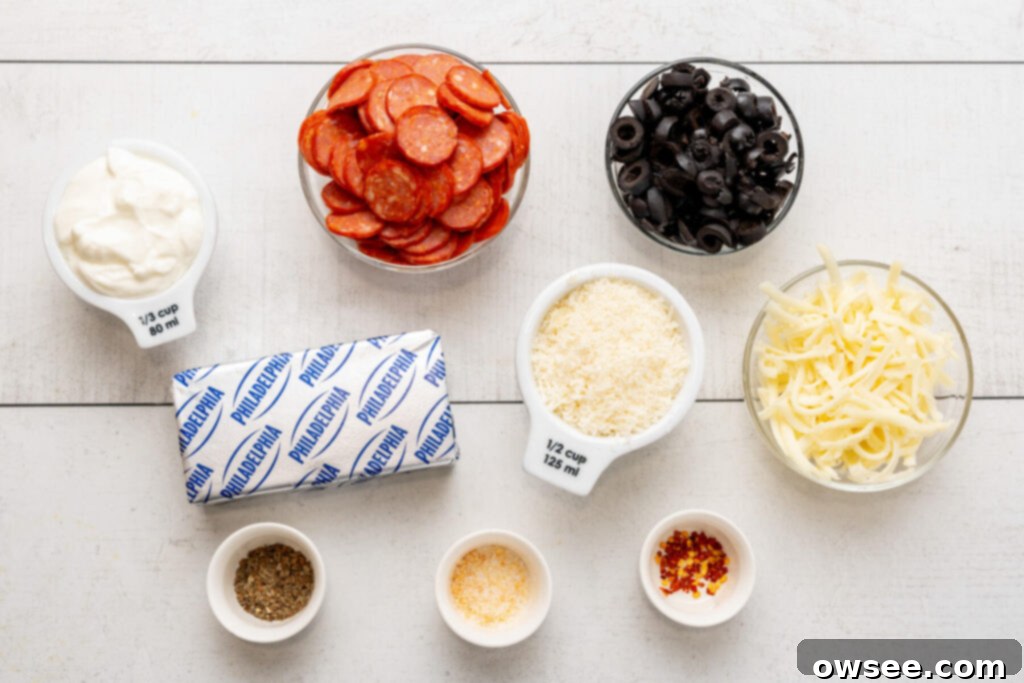 Hot Cheesy Pepperoni Dip 6 Ingredients needed to make pepperoni dip, neatly arranged: sour cream, a pile of mini pepperoni, a small bowl of sliced black olives, a block of cream cheese, shredded parmesan cheese, shredded mozzarella cheese, a container of Italian seasoning, garlic salt, and crushed red pepper flakes.
