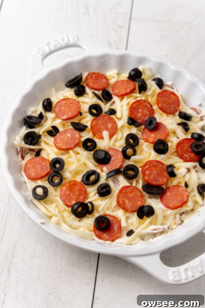 Hot Cheesy Pepperoni Dip 9 A pie plate filled with the pepperoni dip mixture, topped with shredded mozzarella, reserved pepperoni slices, and black olives, ready to be baked.
