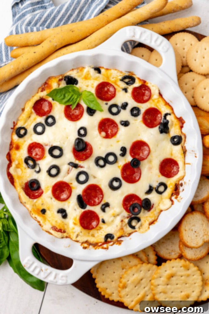 Hot Cheesy Pepperoni Dip 10 A baked pie plate of hot pepperoni dip, golden and bubbly, sits next to a serving tray laden with a variety of dippers like crackers and breadsticks.