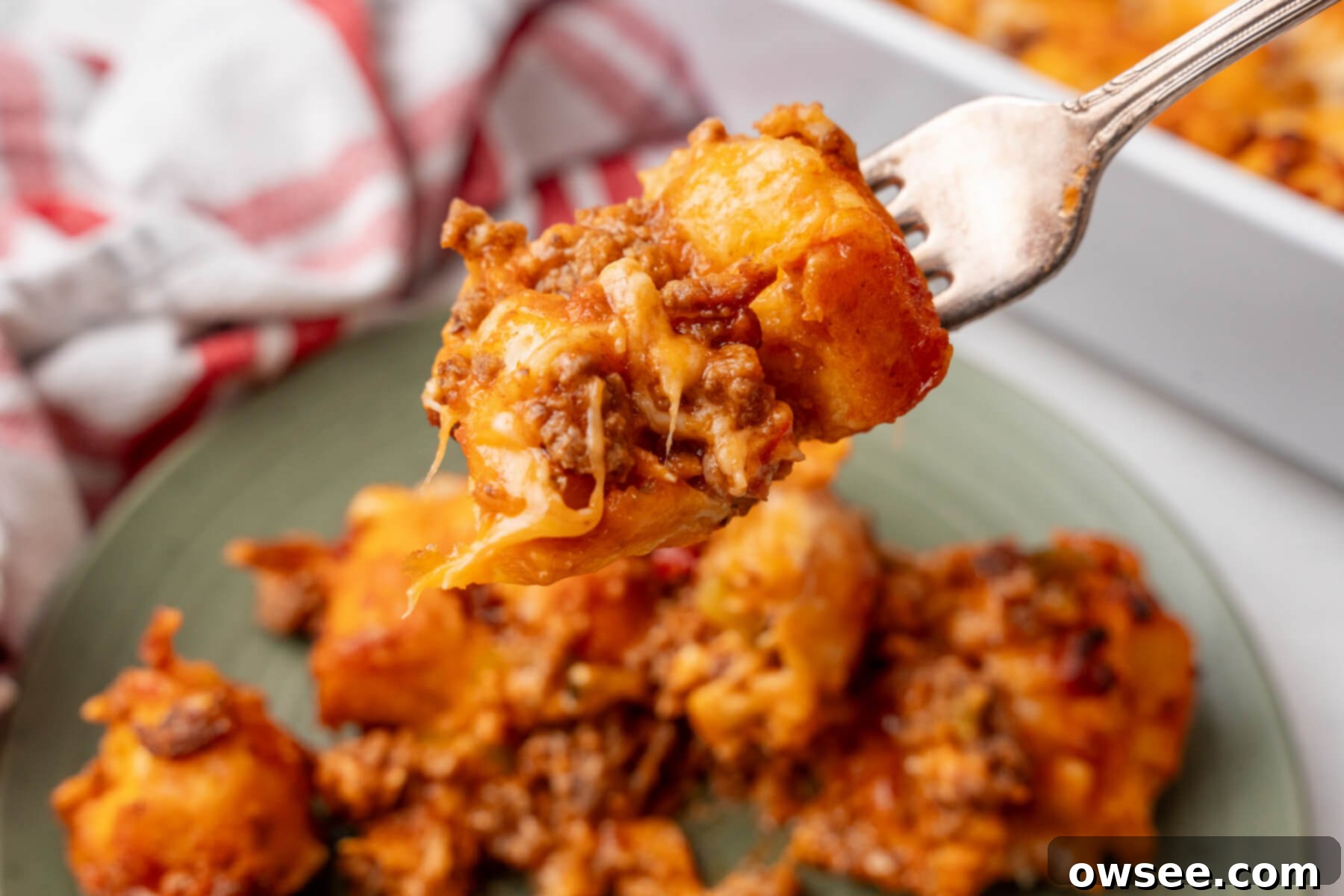 A fork with a bite of Sloppy Joe Biscuit Casserole above a plate, showing the cheesy, saucy interior and fluffy biscuit topping.
