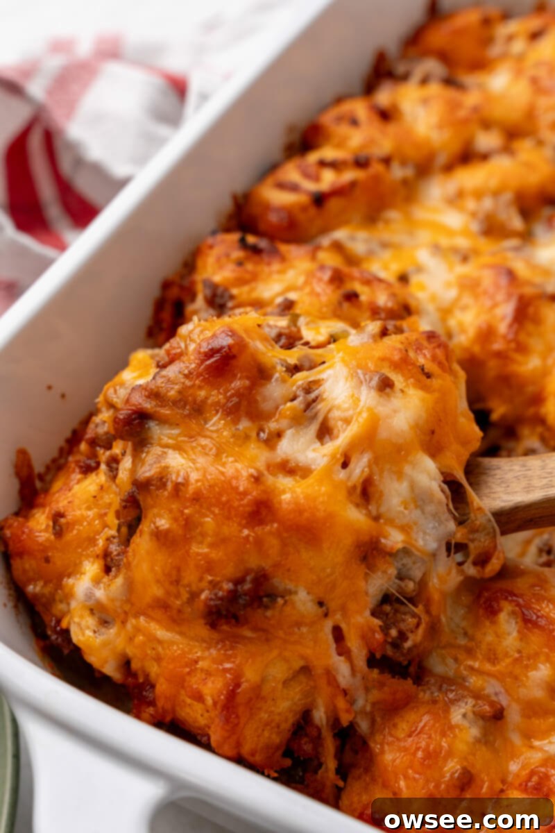 A wooden spoon taking a scoop out of the golden-brown sloppy joe biscuit casserole, revealing the saucy interior.