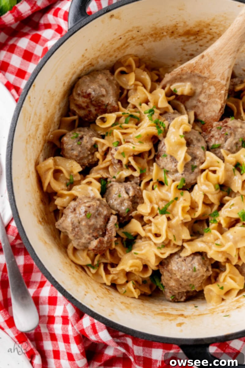 Creamy One Pot Swedish Meatballs and Noodles 3 A pot of finished Swedish Meatballs and noodles stirred with a wooden spoon, showcasing the creamy sauce.