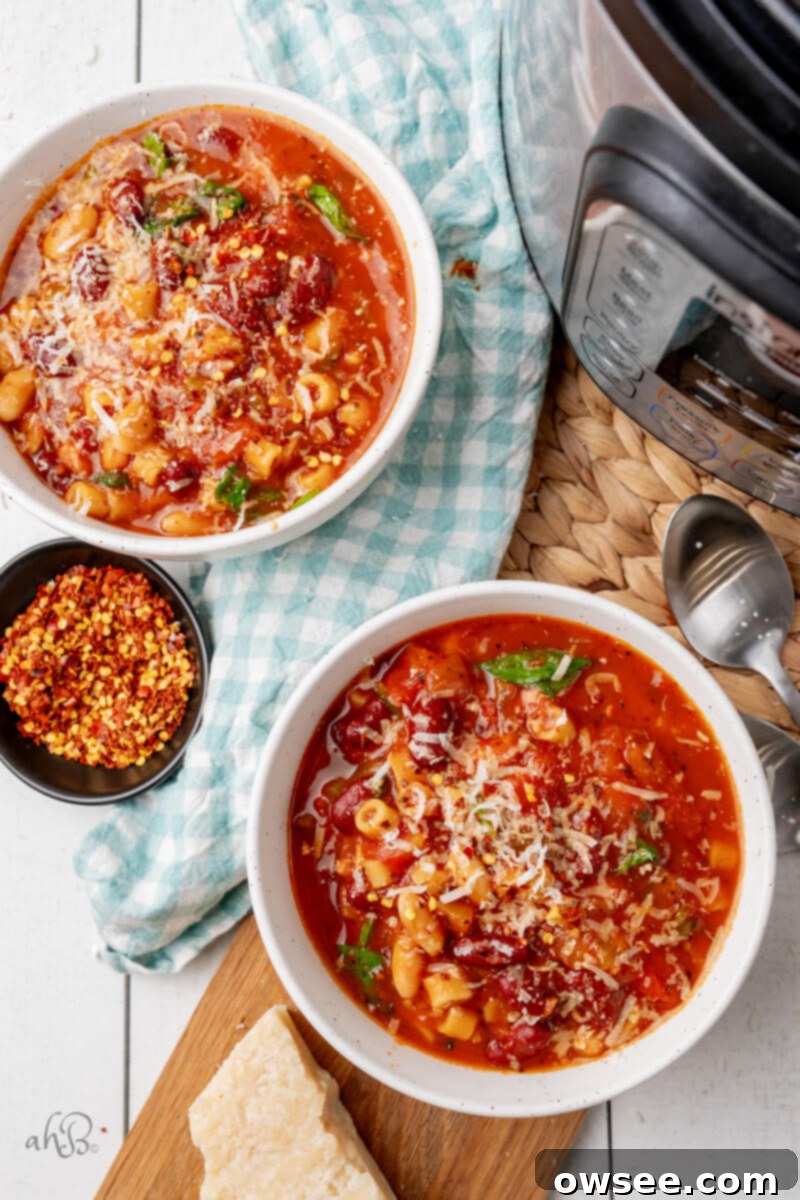 Hearty Instant Pot Minestrone Soup 4 Two white bowls filled with Minestrone Soup topped with parmesan cheese and pepper flakes, sitting next to the instant pot.