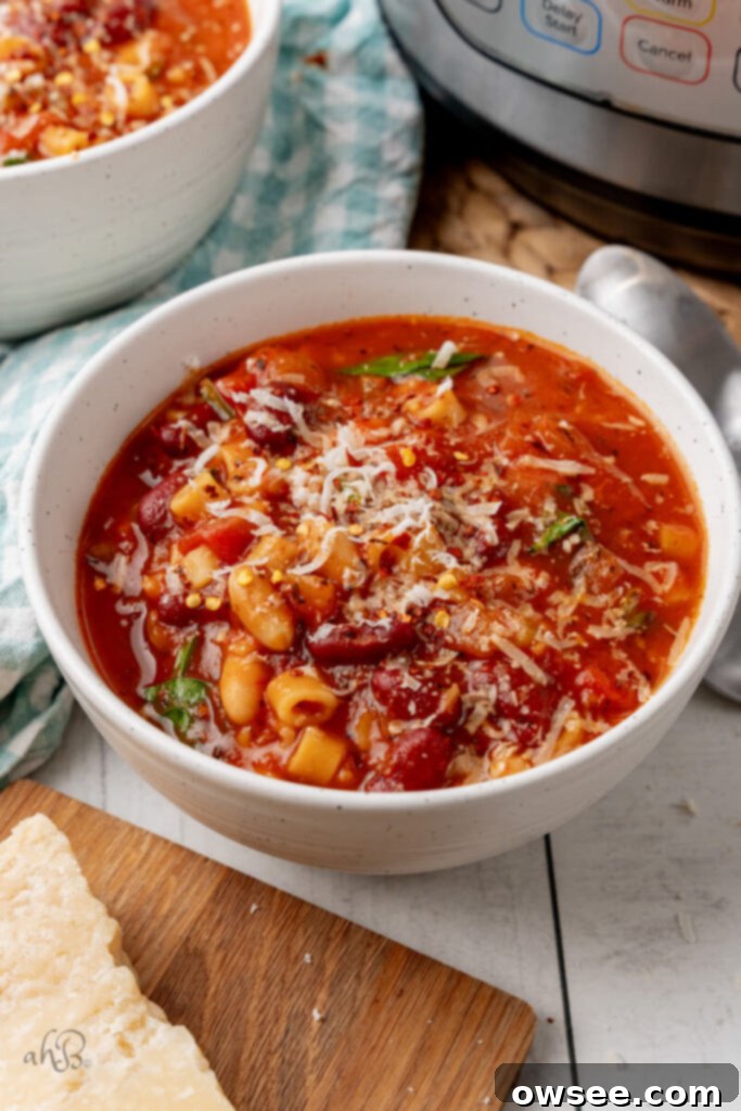 Hearty Instant Pot Minestrone Soup 9 A white bowl of Minestrone Soup is topped with parmesan cheese and chili flakes.