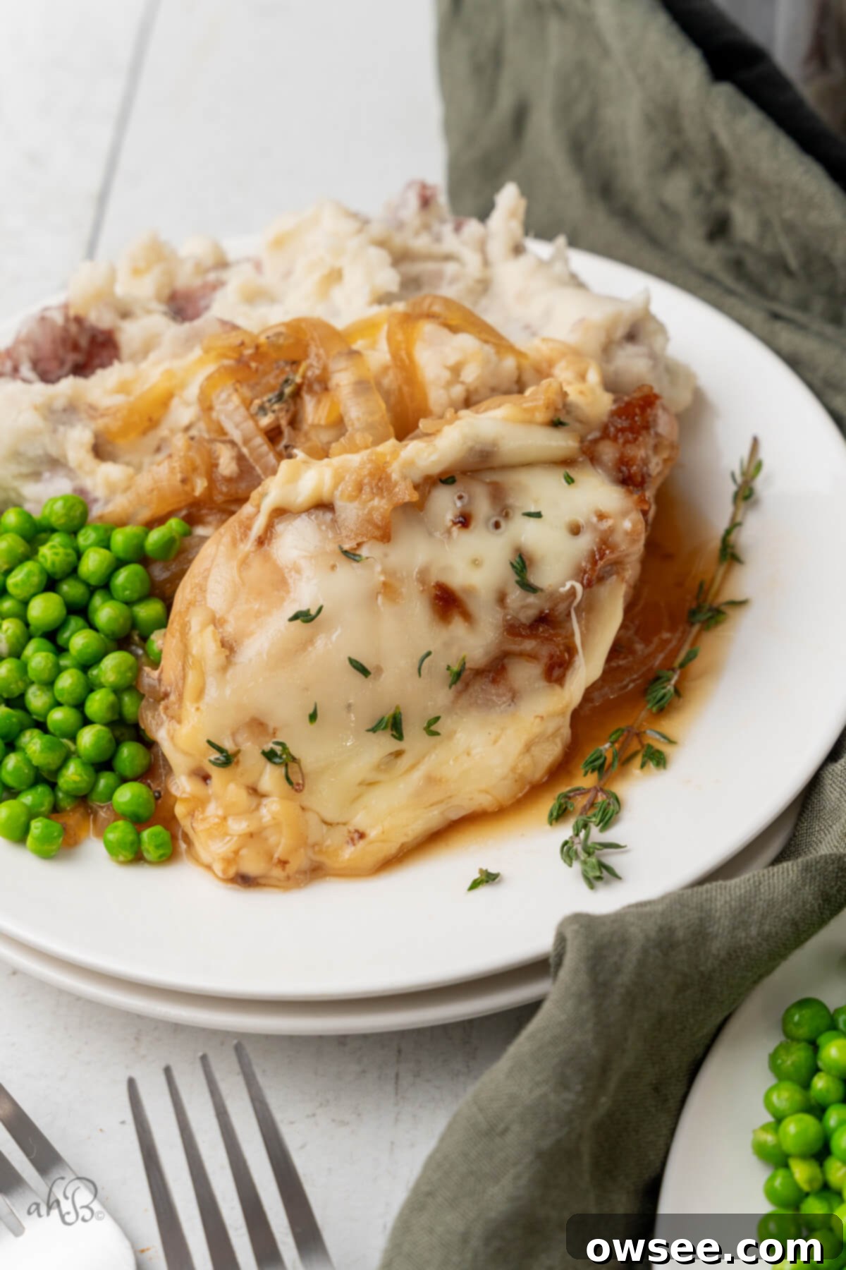Slow Cooker French Onion Chicken 2 A serving of French Onion Chicken with peas and mashed potatoes on a white plate.