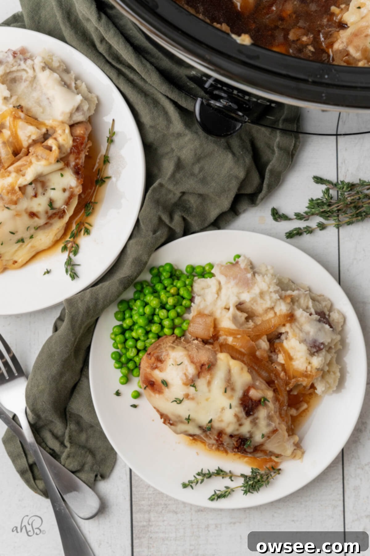 Slow Cooker French Onion Chicken 3 Two plates of French Onion chicken, mashed potatoes, and peas, served on white plates next to the crockpot.